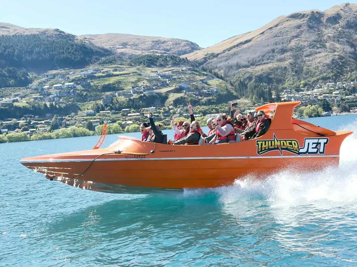 Un jet boat orange filant sur le lac Wakatipu sous des montagnes enneigées